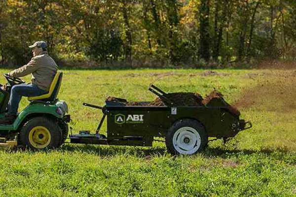 A riding lawn mower pulling a compact manure spreader.