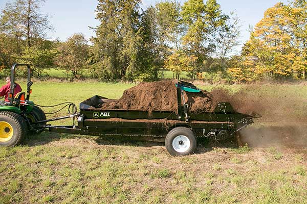 A 185 ft³ PTO Manure Spreader spreading manure on a field in the fall