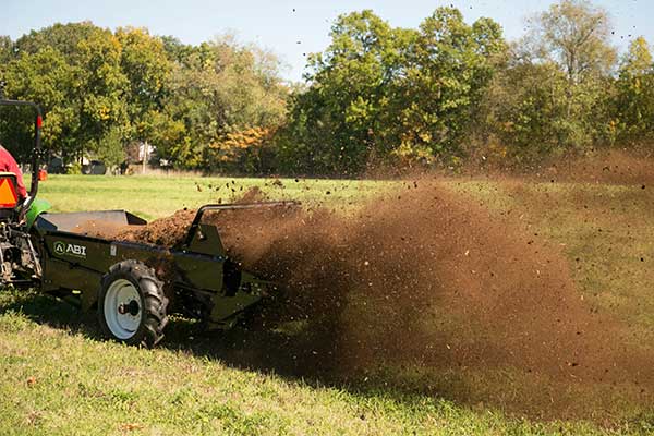 The wide and fine spreading spray of a PTO manure spreader from behind.