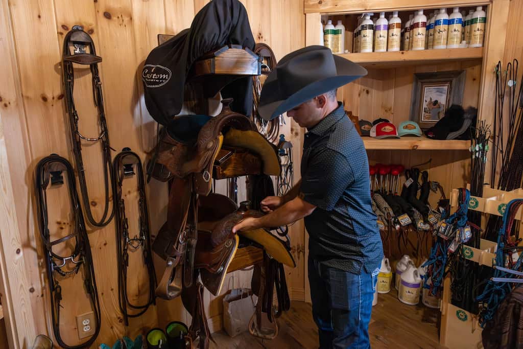 DragMaster Horizon Luke holding the front of a saddle in a tack room
